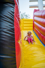 Fototapeta na wymiar Cute blonde girl riding an inflatable slide.