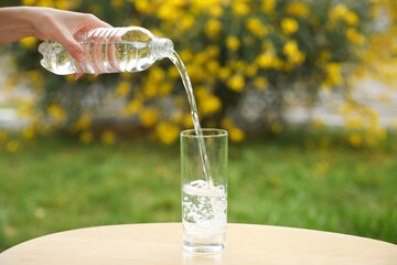 Woman pouring water from bottle into glass on table outdoors, closeup