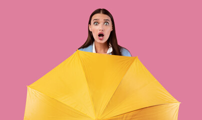 Portrait of shocked girl holding yellow umbrella at studio © Prostock-studio
