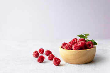 Fresh raspberries and leaves in a wooden bowl with soft plain pink purple background and copy space