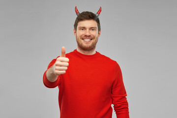 holiday, theme party and people concept - happy smiling man in halloween costume of devil showing...