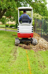 Workman using a mini digger to excavate a hole in the garden. Czech republic, Europe.