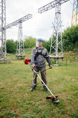 A young man mowing grass on the territory of an electric substation in overalls. Grass cleaning at...
