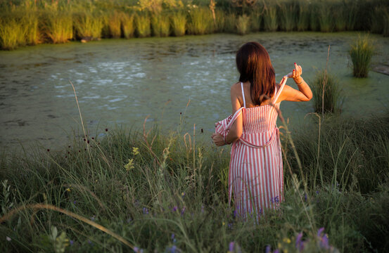 A beautiful girl with dark hair stands on the Bank of a pond. The woman is going to bathe, she undresses. Vintage rural life.