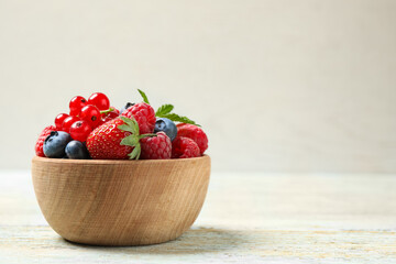 Mix of different fresh berries in bowl on wooden table. Space for text