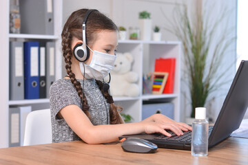 Schoolgirl in a medical mask and headphones with a microphone doing homework at home or studying in class at a lesson at school.Student safety after covid-19 pandemic. Back to school.Distance learning