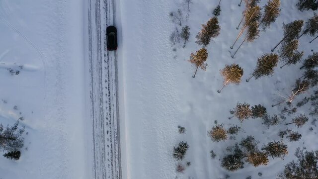 Aerial view of car driving on winter road passing woods and trees getting to wanderlust destination, bird's eye view of road trip on 4x4 trip driving on off road for discover journey
