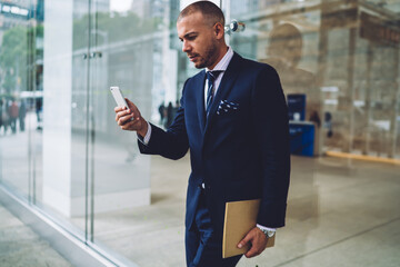 Serious businessman in elegant suit reading messages on smartphone sending feedback while walking,pensive executive manager checking calendar notification in mobile application planning