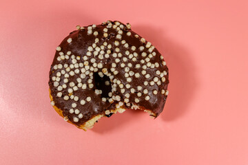 Bitten tasty chocolate donut on a pink background. Top view