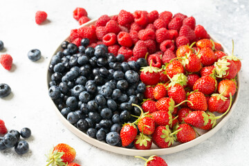 Fresh berries. Different berries in a white ceramic plate on a light table. Strawberries, raspberries and blueberries on a plate. Berries close up