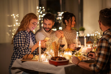 holidays and celebration concept - happy friends with smartphone having christmas dinner party at home