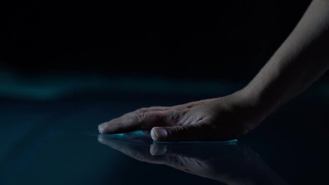 woman is touching dark blue water in pool in darkness, closeup