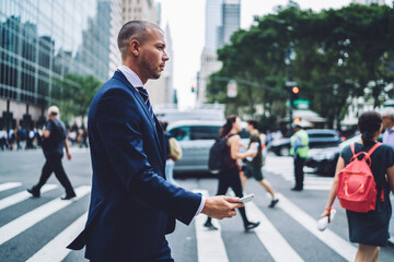Side view of confident businessman passing crosswalk in modern district of megalopolis choosing direction, serious male entrepreneur crossing street with crowd getting to office building by foot. - Powered by Adobe