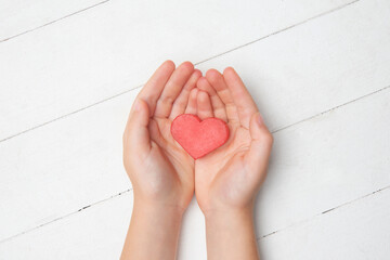 Human hands holding, giving heart isolated on white wooden background. Concept of emotions, feelings, charity, family, supporting hand. Thankful, inspirational. Romantic and togetherness.