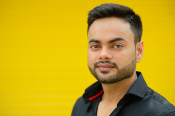 Young handsome bearded Indian businessman against yellow background