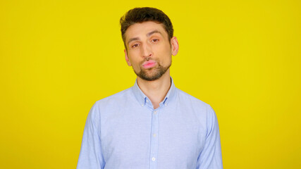 Handsome bearded man kisses on yellow background with copy space. Sexy guy in light blue shirt. Place for text or product