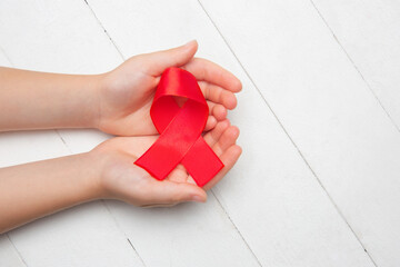 Female and male hands holding red HIV and AIDS awareness ribbon isolated on wooden background. Concept of healthcare and medicine, worldwide supporting, volunteer campaign against illness.