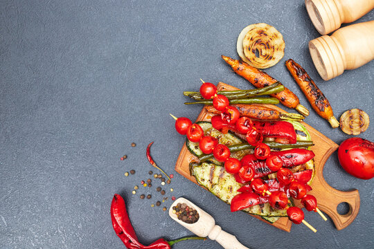 grilled vegetables on a wooden board on a black table, copyspace, flatley