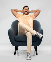 people and furniture concept - happy smiling young indian man sitting in chair over grey background