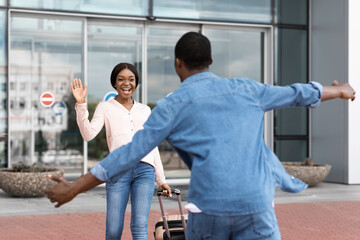 Happy african girl meeting her boyfriend after landing in airport, waving hand