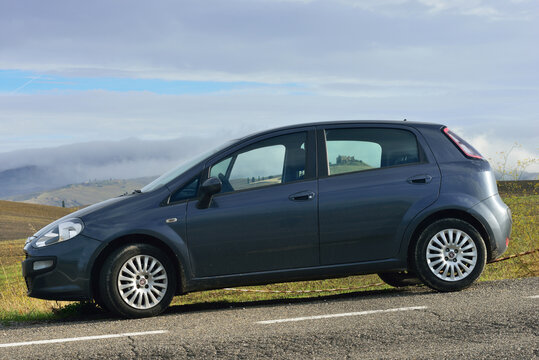 Pienza, Italy - October 13, 2012: Fiat Punto Evo car parked in front of wonderful landscape with hills with autumns grain fields and old castle seen through windows of car. World famous Vall d'Orcia