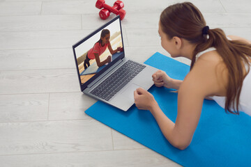 Home workout. Young girl making elbow plank to online fitness tutorial on laptop. Fit woman exercising to sports video