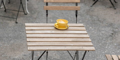 yellow empty cup for coffee on wooden surface of street cafe table