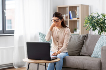 remote job, business and vision concept - tired young woman in glasses with laptop computer working at home office and rubbing her eyes