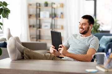 technology, remote job and lifestyle concept - happy smiling man with tablet pc computer and earphones resting feet on table at home office