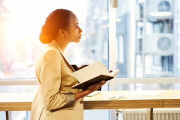 Portrait of mindful talented creative manager of event company thinking over new projects concept noting ideas into personal organizer while making remote job communicating with executive on phone