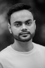 Young handsome bearded Indian man at the park in black and white