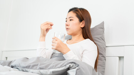 Sick Asian holding a glass of water and taking medicines from headache, Healthcare uses medicine concepts.