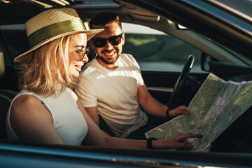 Happy Young Couple Sitting Inside Their Car, Man and Woman Using Map on Road Trip, Travel and Adventure Concept