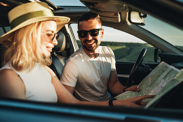 Happy Young Couple Sitting Inside Their Car, Man and Woman Using Map on Road Trip, Travel and Adventure Concept