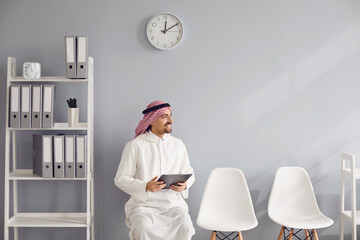 Arab worker is waiting for an interview with a resume in hands sitting on a chair in the office.