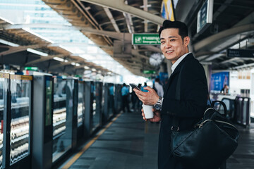 Smiling business man holding a disposable coffee cup and phone at train station stock photo