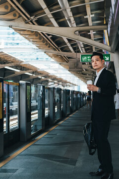 Business man holding a disposable coffee cup and waiting at train station stock photo