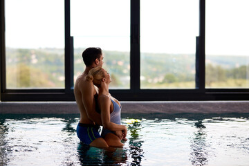 Embraced couple standing in the pool and enjoying the view at the spa.