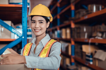 Asian woman wearing a hardhat standing cargo at goods warehouse and check packaging for control loading from Cargo freight ship for import and export by report on tablet. Teamwork concept