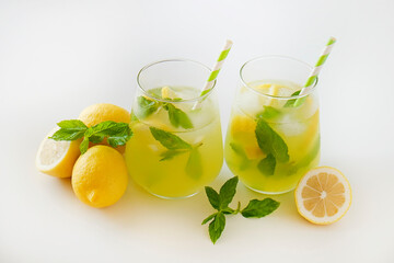 Two glasses of refreshing non alcoholic mojito drink with lemon slices, mint leaves and ice. Studio shot of iced lemonade isolated on white background, close up, copy space.