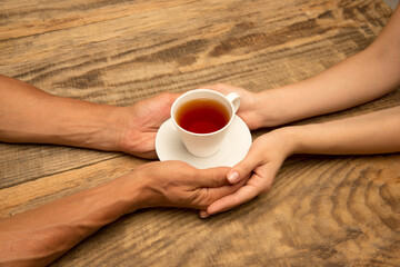 Hands of couple holding mug of tea, top view on wooden background with copyspace. Drinks, home comfort, warm event and evening, coziness with family. Copyspace for advertising.