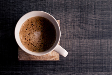 Close up of a white cup of coffee at a grey wood table