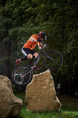 Front view of man holding a bicycle handlebar and doing a stunt over stones. Athlete trying to land...