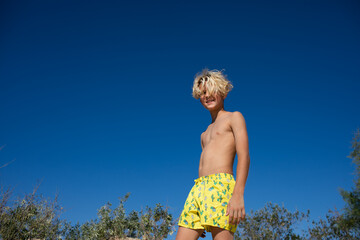 Young teen boy in yellow swim shorts posing on a sand hill at the beach. Copy space. © Alina