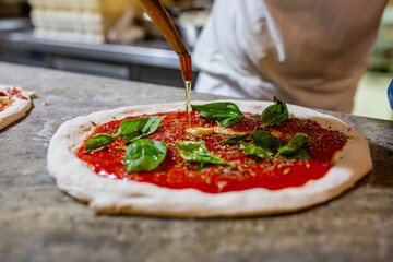 Pizzaiolo mentre condisce con l'olio una pizza marinara napoletana 