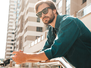 Portrait of handsome confident stylish hipster lambersexual model.Man dressed in green shirt. Fashion male posing in the street at skyscraper background in sunglasses