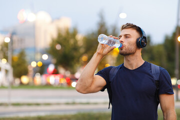 Young sports man making break and drinking water after jogging