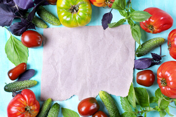 Tomatoes of different sorts, cucumbers and basil leaves are framing the copy space on the piece of craft paper