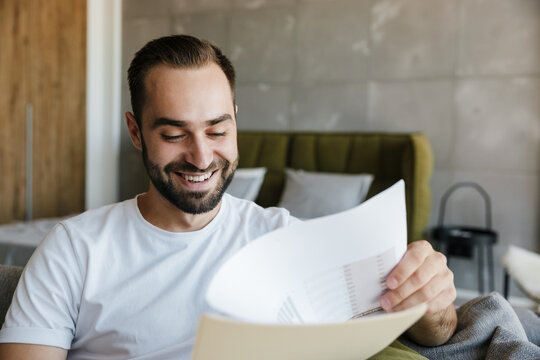 Image of young joyful man working with papers while sitting on couch
