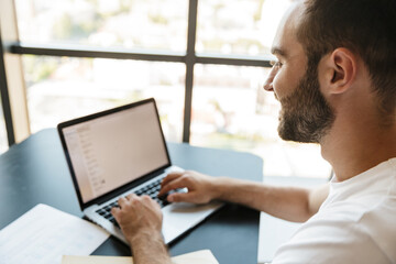 Image of cheerful man working with laptop while sitting at table